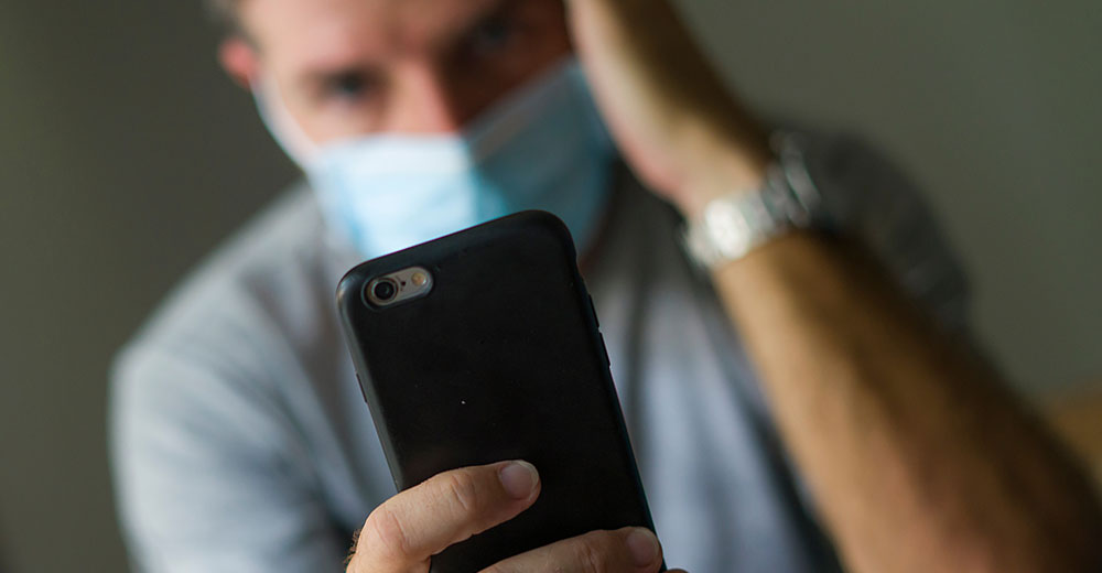 man with face mask in home quarantine lockdown checking pandemic news